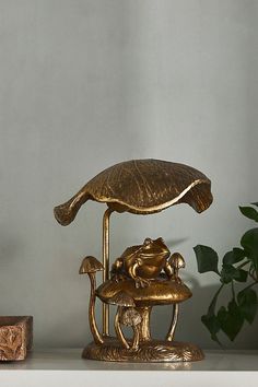 a gold frog lamp sitting on top of a table next to a potted plant