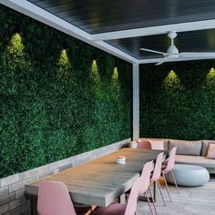 an outdoor dining area with wooden tables and pink chairs, surrounded by green wall panels