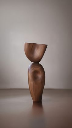 a wooden vase sitting on top of a table next to a white wall and floor