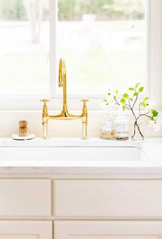 a kitchen sink with gold faucet and white countertops in front of a window