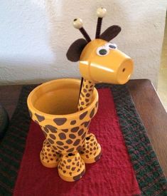 a giraffe shaped cup sitting on top of a red tablecloth next to a stuffed animal