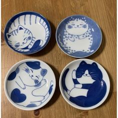 four blue and white plates with cats on them sitting on a wooden table next to each other