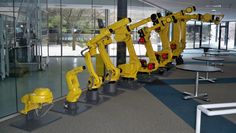 some yellow robots are lined up in a room with glass walls and tables on either side