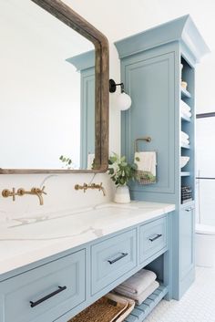 a bathroom with blue cabinetry and white counter tops, along with a large mirror above the sink