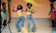 two women in yellow shirts and blue jeans are dancing