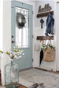 a vase with flowers sitting on the floor next to a blue door and some hooks