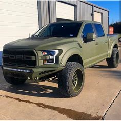 a green truck is parked in front of a building with two large tires on it