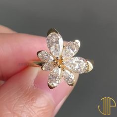 a close up of a person's hand holding a flower shaped diamond ring