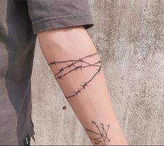 a person with a tattoo on their arm holding a cell phone and barbed wire behind them