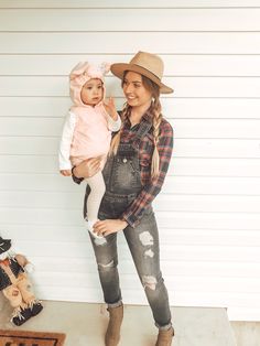 a woman in overalls and cowboy hat holding a baby girl wearing a pink outfit