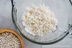 a glass bowl filled with white beads next to a wooden bowl full of brown and white seed