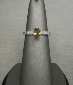 a ring with a yellow and white diamond in it sitting on top of a silver stand