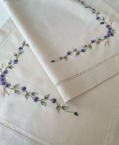 two white sheets with blue flowers and green leaves embroidered on the edges, sitting next to each other