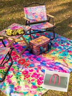 two chairs and a table with fruit on it in the grass next to a picnic blanket