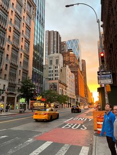 a busy city street with cars and people walking on the sidewalk at sunset or dawn