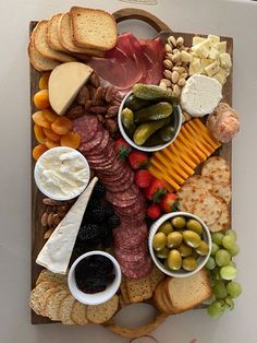 a wooden platter filled with different types of cheeses, crackers and meats