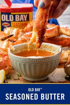 someone dipping some food into a bowl with crab legs in it and the caption old bay seasoned butter