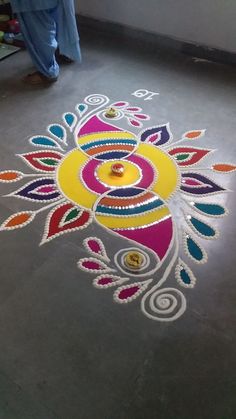 a colorful rangdi design on the floor in front of a person standing next to it