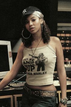 a woman standing in front of a mixing desk with headphones on her ears and wearing a tank top that says get it up bob marley