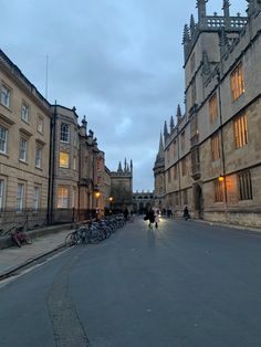 people are walking down the street in front of some old buildings at dusk with their bikes parked on the side