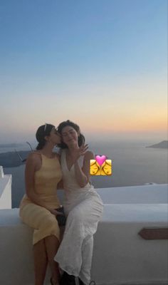 two women sitting next to each other on top of a roof with the ocean in the background