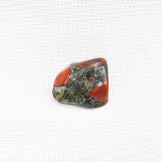 a piece of red and green rock sitting on top of a white surface