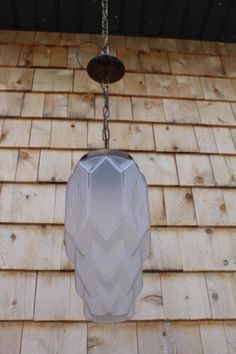 a white vase hanging from a chain on top of a wooden wall next to a light fixture