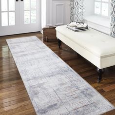 a white bench sitting on top of a hard wood floor next to a window covered in curtains