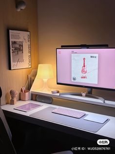 two computer monitors sitting on top of a desk in front of a lamp and pictures