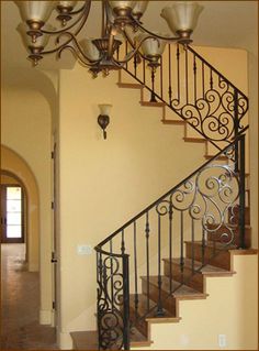 a staircase with wrought iron railing and chandelier in an empty home entryway