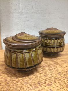 two ceramic jars sitting on top of a wooden table