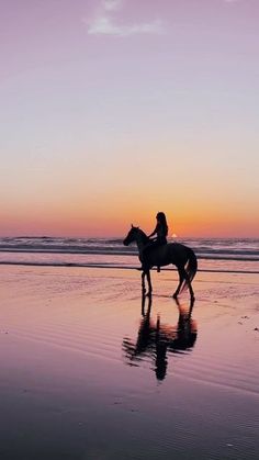 a person riding a horse on the beach at sunset