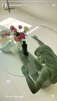 a glass table topped with a vase filled with flowers next to a small statue on top of it