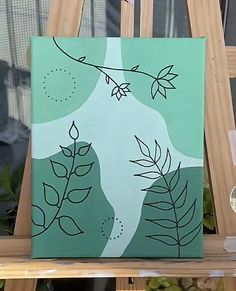 a painting is sitting on a wooden easel in front of a window with green leaves