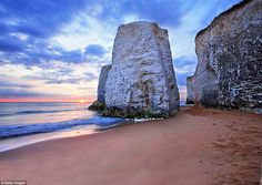 the sun is setting behind two large white rocks on the beach near the water's edge