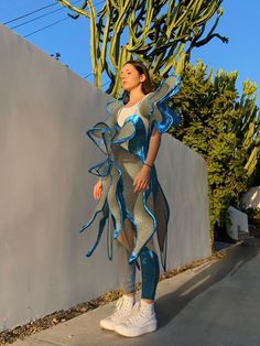 a woman dressed in blue and silver standing next to a cactus tree with her hands on her hips