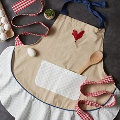 an apron, spoon and eggs on a table with other kitchen accessories including utensils