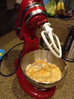 a red mixer sitting on top of a counter next to a bowl filled with food