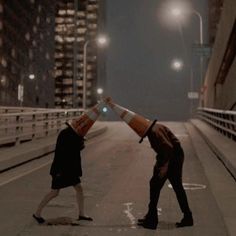 two people standing on the side of a road with traffic cones over their heads in front of them