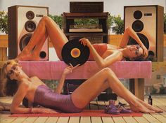 two women in bathing suits laying on top of a table with speakers and record players