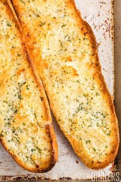 two pieces of bread sitting on top of a baking pan covered in cheese and herbs