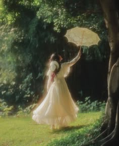 a woman in a white dress holding an umbrella next to a tree and grass field