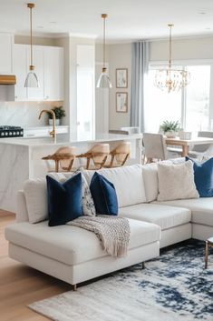 a living room with white couches and blue pillows on the floor in front of a kitchen