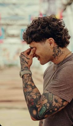 a man with lots of tattoos on his arm and shoulder holding his hand to his face