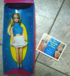 a barbie doll in a box next to a card and sticker on the floor