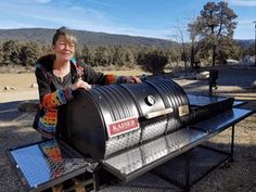 a woman standing next to a large metal barrel on top of a table in the middle of a field