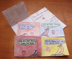 four children's handmade note cards on a wooden table with paper attached to them