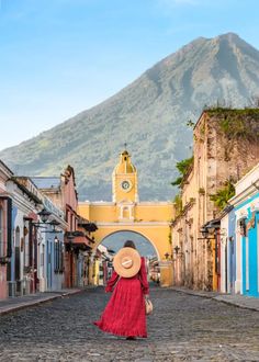 a woman in a red dress and hat walks down an old cobblestone street