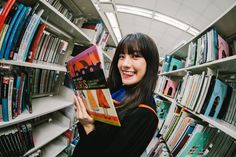 a woman holding up a book in front of bookshelves