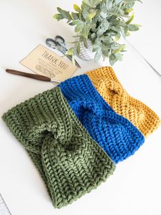 three knitted scarves sitting on top of a white table next to a plant